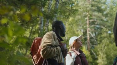 Sırt çantaları taşıyan, çoklu etnik çeşitliliğe sahip yürüyüşçülerin, verimli yeşilliklerle çevrili güneşli günlerinin keyfini çıkardıkları orta derece yavaş bir çekim.