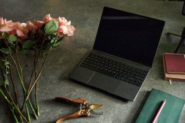 Açık dizüstü bilgisayarın açık arkaplan kompozisyonu. Düşük ışık fotokopi alanında desenli koyu masa üzerinde çiçekler.