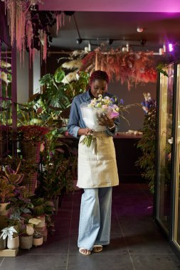 Çiçekçide çalışırken elinde güzel bir buket tutan Afro-Amerikan kadının dikey portresi.