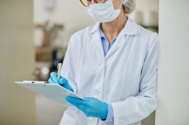 Kadın imalat müdürünün ilaç fabrikasındaki izleme sonuçlarını not defterine yazıp kopyaladığı görüntüler.