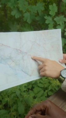 Yeşil ormanda yaz yürüyüşü sırasında kağıt harita üzerinde güzergahı tartışan iki tanınmayan çatlağın dikey görüntüsü