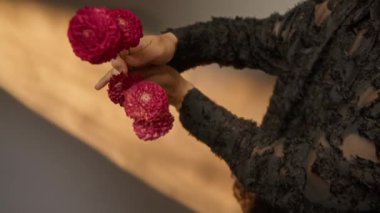 Tanınmayan eller parlak çiçekleri hafifçe aydınlatılmış, aydınlık duvarlara doğru tutarak estetik bir hava ve huzurlu bir atmosfer yaratıyor.