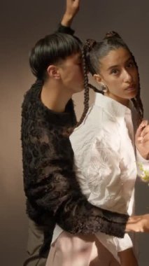 Bir buket taze çiçekle dikey genç çiftin doğal stüdyo arkaplanındaki kameraya çağdaş dans figürleri sergilediği orta boy bir fotoğraf.