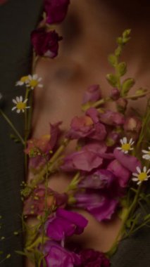 Odaklanmış ön planda güzel kır çiçeklerinin dikey yakın çekimi ve bulanık arka planda narin bir kadının narin göğsü.