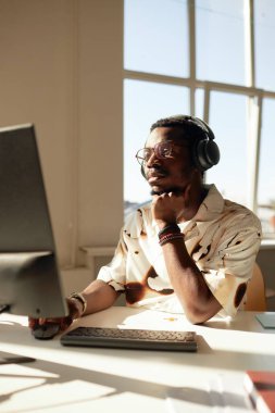 Afrika kökenli Amerikalı bir adamın güneş ışığıyla aydınlatılmış ve bilgisayar kullanılarak iş gününün keyfini çıkardığı dikey sıcak ton portresi.
