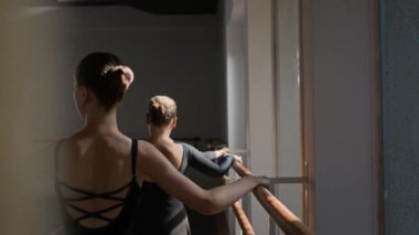 Modern dans stüdyosunda performans için prova yapan üç bale dansçısının bar ekipmanları ve antrenör yardımı ve desteği ile aşağı doğru çekimini yapın.