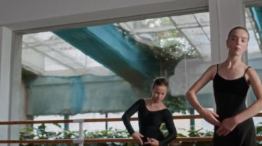 İki beyaz kadın bale dansçısı performans provası yaparken güneşli stüdyo boyunca zarif bir şekilde ilerliyorlar.