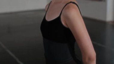 Modern sınıfta kolları arkasında parke zemin ve beyaz duvarlarla siyah taytlı genç beyaz kadın balerin portresini yukarı kaldır.