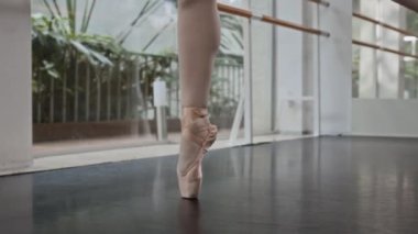 Beyaz tayt ve ipek ayakkabılar giyen zarif balerin stüdyo zemininde bale hareketleri yapıyor.