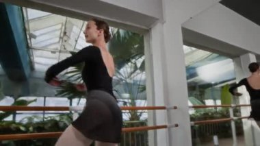 Siyah taytlı zarif genç bir kadının, geniş stüdyoda piruetlerle güzel bir bale dansı yaptığı yavaş çekim.