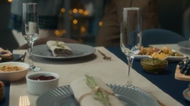 Tanımlanamayan bir çiftin evde sıcak bir Noel kutlaması için yemek masasında salata ve ana yemek servisi yaptığı sahneler.