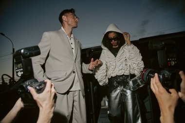 Göz kamaştırıcı Orta Doğu 'lu kadın ünlülerin özel hayatı için kaputu çekerken, paparazzilerin arabadan inerken yakaladığı düşük açılı fotoğraf. Yanında da şehirdeki gece caddesinde iyi giyimli bir adam var.