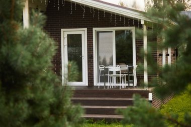 Background image of cute suburban house with patio shot through evergreen fir trees in front yard copy space clipart