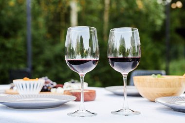 Kapalı arkaplan görüntüsü iki kırmızı şarap bardağı açık hava yemek masasında, beyaz bez kopya alanı ile hazırlanmış.