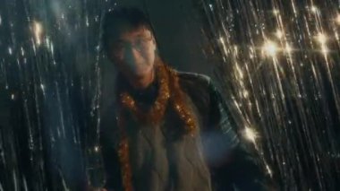 Genç, neşeli Asyalı adam boynundaki süslemelerle kameraya poz veriyor gümüş folyo perdelerine karşı, Noel partisinde