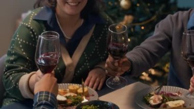 Memleketteki sıcak Noel ziyafeti için masanın etrafında toplanırken kadehlerini kadeh tokuşturan çeşitli arkadaşların yavaş çekimleri.
