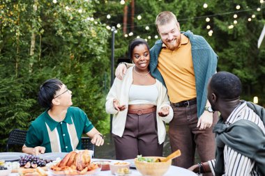 Yeşil bahçede sohbet eden ve eğlenen çok ırklı yetişkin arkadaş grubunun renkli görüntüsü