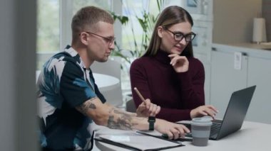 Beyaz mobilyalar ve geniş pencerelerle dizayn edilmiş minimalist çalışma alanındaki dizüstü bilgisayarla proje fikirlerini tartışan genç beyaz özgür çiftlerin belini kaldırın.