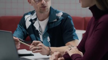 Kafe masasında dizüstü bilgisayar başında konuşan, gözlüklü, yaratıcı, genç ve beyaz bir çift.