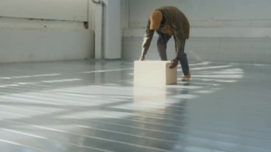 Genç siyahi adamın portresi karton kutuyu yerden kaldırıyor, güneş ışığıyla aydınlanan geniş bir depoda duruyor ve kameraya bakıyor.