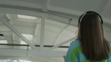 Geniş bir depo odasında yürürken, kulaklıklı, ağır kutular taşıyan beyaz bir kadının, hareket halinde olduğunu gösteren bir fotoğraf.