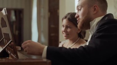 Zarif formalı genç aristokrat kız erkek öğretmenle müzik dersi alıyor Viktorya dönemi ortamında klasik piyanonun başında oturuyor.