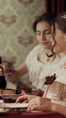 İki asırlık aristokrat genç kadının dikey bel üstü pozu. Çayın tadını çıkarırken böğürtlenlerle süslenmiş klasik yemek masasında oturuyorlar.