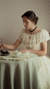 19. yüzyılın aristokrat genç kadınının dikey orta pozu. Klasik ortamda zarif bir masada oturmuş, kağıt üzerine mürekkep kalemle mektup yazarken.