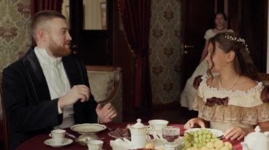 19. yüzyılda zarif giyinmiş güzel beyaz bir kadının iki aristokrat insanı selamladığı orta boy bir fotoğraf. Onlar yemek masasında oturmuş, öğleden sonra sohbet ederken.