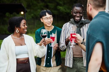 Çeşitli yetişkin grupları bardaklarını içerken dışarıda kutlama yapıyor ve bayramı dışarıda kutluyorlar.