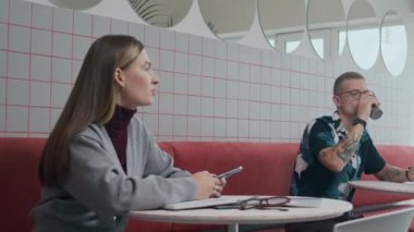 Kahve molası sırasında minimalist tasarım kafeteryasında küçük yuvarlak masalarda otururken orta boy Kafkasyalı birkaç meslektaşın konuşması.