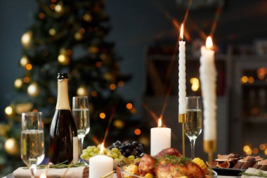 Noel kutlaması için süslenmiş şenlikli tabaklar ve şampanya bardaklarıyla yemek masasındaki yanan şamdanı kapat.