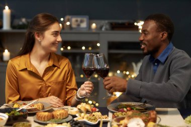 Gülümseyen zenci bir adamın romantik bir randevuda şarap kadehlerini tokuşturması ya da oturma odasında yemek masasında otururken Noel kutlaması yapması.