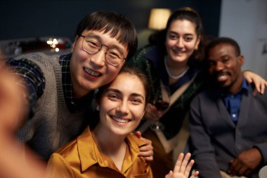 Portrait shot of joyful woman smiling at camera while taking selfie with four cheerful friends clipart