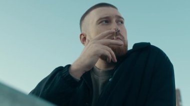 Sakallı, açık mavi gökyüzünün altında sigara içerken olayın detaylarını ve ipuçlarını düşünen Kafkas polis memurunun alçak açısı.