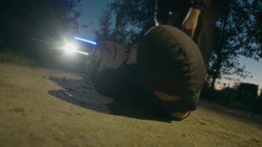 Polis memuru siyah kar maskeli silahsız suçluya kelepçe takıyor ve gece tutuklaması sırasında polis arabasına doğru çekiliyor.