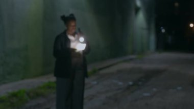 Fidye notu ve el feneri tutan ve gece vakti sokakta dikilen ciddi bir siyahi kadın polis memurunun zoom portresi.