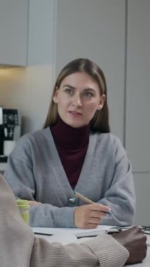 Modern çalışma alanında masada oturan ve beyin fırtınası sırasında tanınmayan siyahi erkek meslektaşının konuşmalarını dinleyen beyaz bir kadının dikey belden yukarı çekimi.