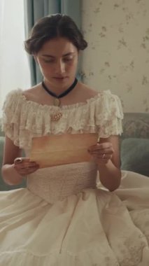 Parşömen kağıdına yazılan mektupla kötü haber aldıktan sonra döşeme üzerinde bayılan 19. yüzyıl genç kadınının dikey görüntüsü.