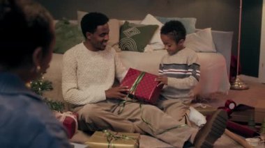 Afrika kökenli Amerikalı çocuğun oturma odasında oturup ailesine Noel için hediye paketlemelerine yardım ettiği bir fotoğraf.