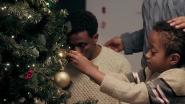 Akşamları Noel ağacını süslerken kocasına ve oğluna sarılan Afrikalı Amerikalı bir kadın.