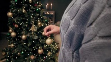 Örgü örüp Noel ağacını altın cam toplarla süsleyen tanınmamış bir kadın.
