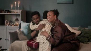 Mutlu Afrika kökenli Amerikalı ebeveynler Noel sabahı oturma odasında kanepede otururken oğullarına sarılıyorlar.