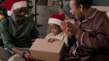 Neşeli genç Afrikalı Amerikalı ebeveynler ve çocuk Noel hediyesini açıyor ve alkışlıyorlar.