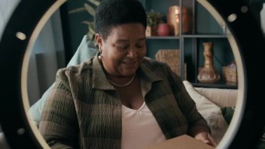 Kıdemli Afro-Amerikan güzellik blogcusu ring lambasının önünde oturmuş boks videosu kaydediyor.