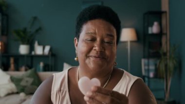 Yüz masajı için kalp şeklindeki Gua sha aletini gösteren yaşlı Siyah Güzellik blogcusunun orta boy yakın çekimi