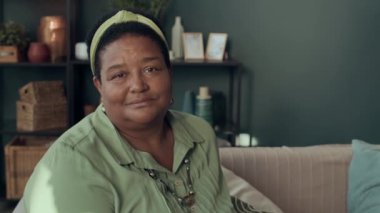 Modern son sınıf Afro-Amerikan kadın portresi şık giyinmiş rahat oturma odasında oturmuş kameraya bakıyor.