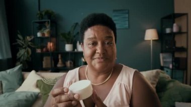 Kıdemli Afro-Amerikan kadın güzellik blogcusu yeni besleyici krem gösteriyor, orta boy yakın çekim.