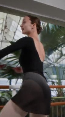 Dikey Slowmo pozunda siyah taytlı zarif genç kadın geniş stüdyoda piruetlerle güzel bir bale dansı yapıyor.