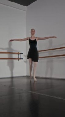 Siyah tayt ve beyaz tayt giymiş zarif bir kızın geniş stüdyoda dans edişinin dikey ve yavaş çekimi.